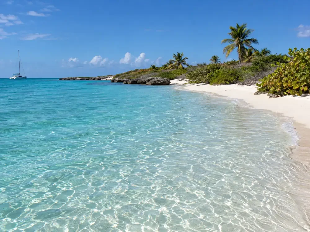 Knietiefes, klares Wasser über weißem Sand an der ruhigen Seite einer kleinen Insel