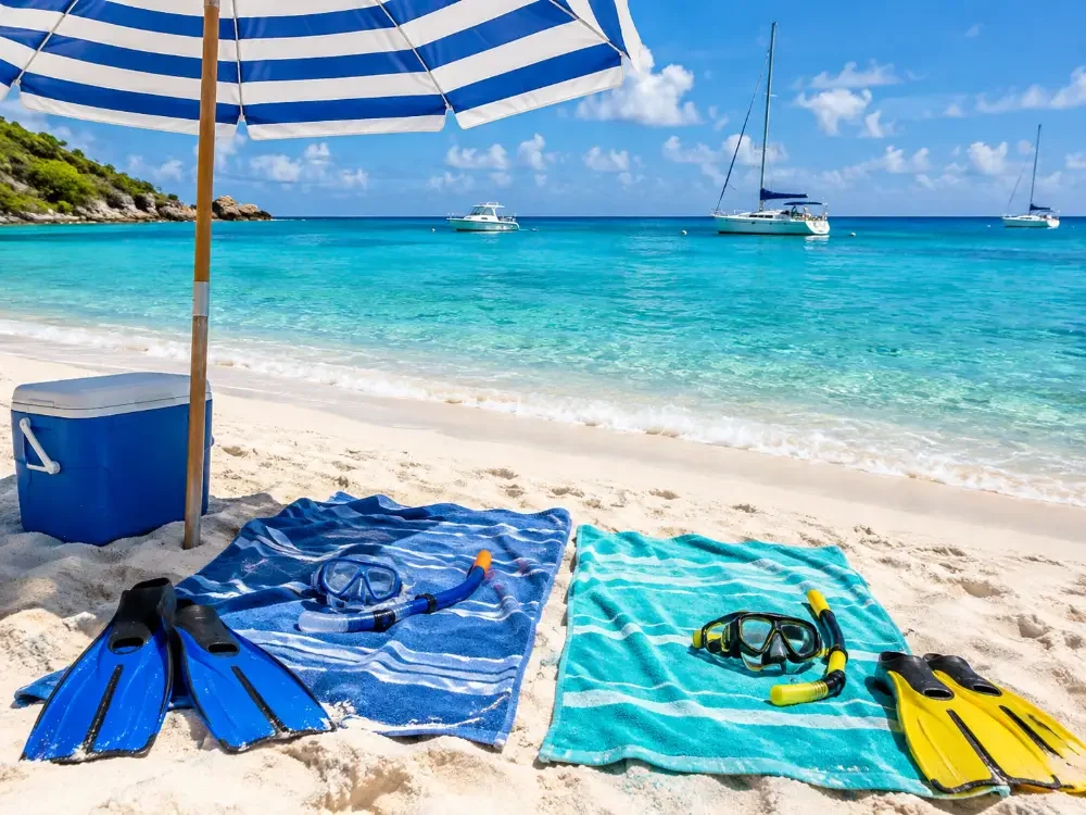 Ein Strandschirm, Handtücher, Schnorchelmasken und eine Kühlbox auf weißem Sand